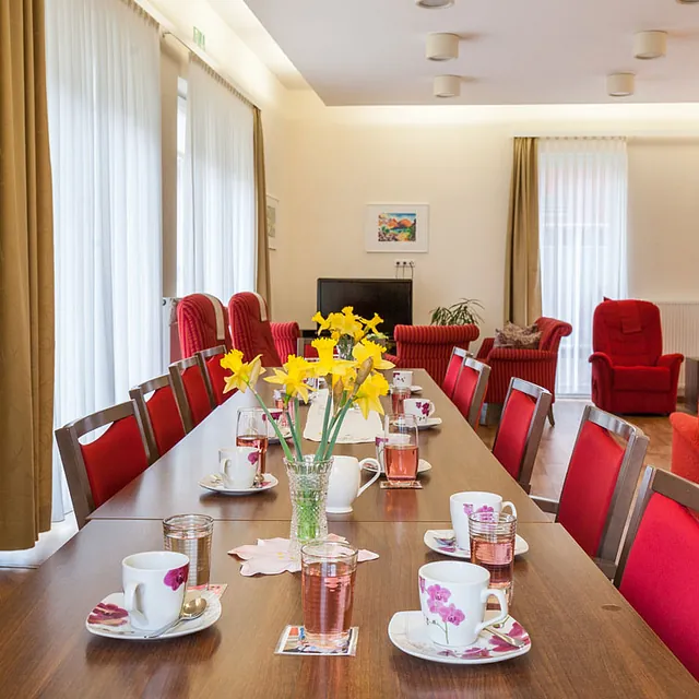Langer Kaffeetisch mit Blumenschmuck im Aufenthaltsraum der Tagespflege Warnemünde.