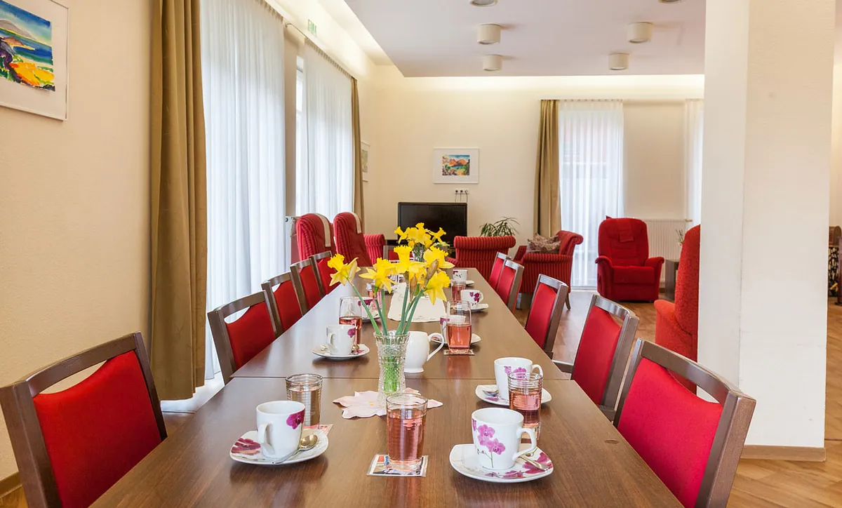 Langer Kaffeetisch mit Blumenschmuck im Aufenthaltsraum der Tagespflege Warnemünde.